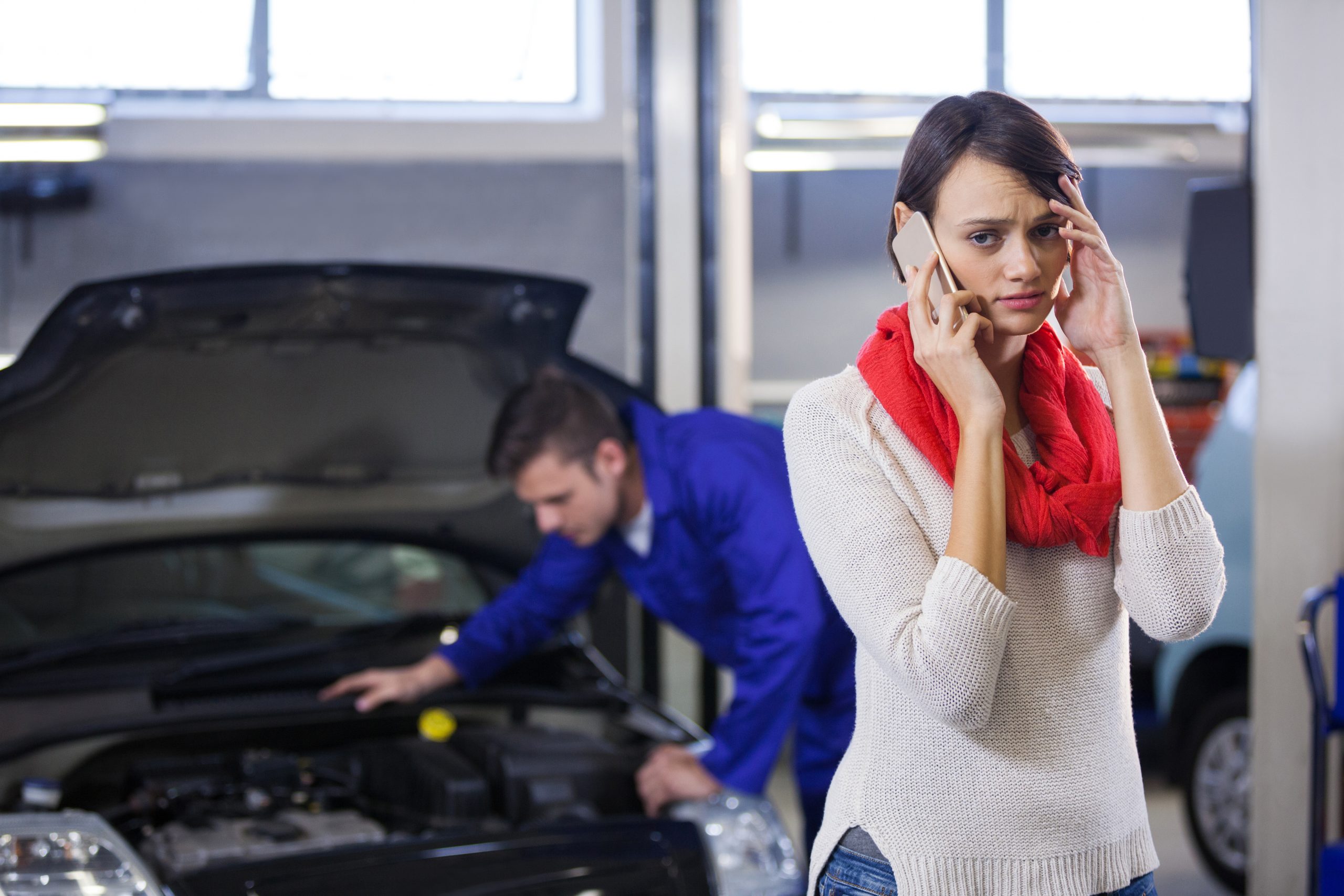 Customer on mobile phone while her car is being repaired in background