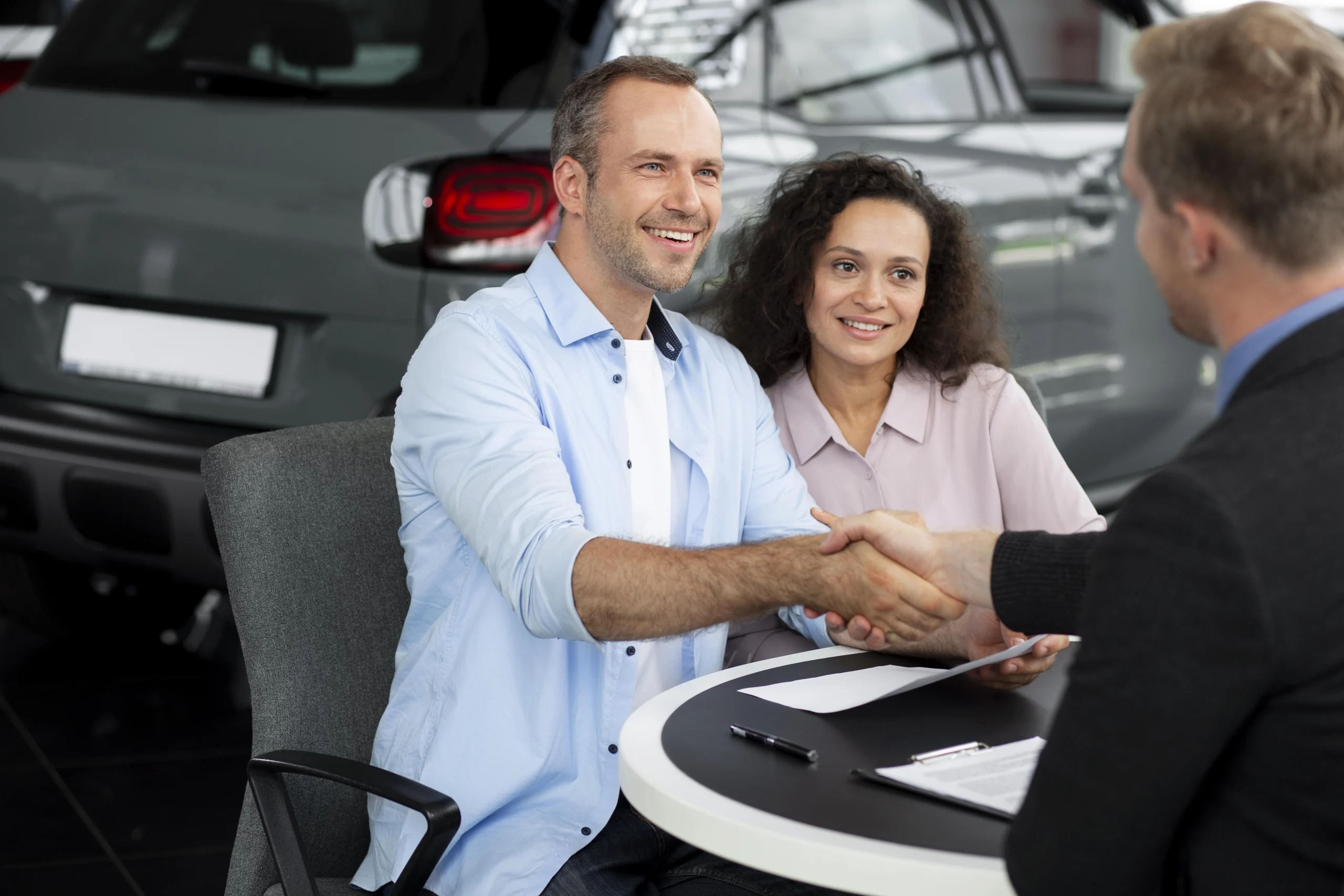 A man and woman shake hands in front of a car, symbolizing a successful vehicle transaction related to Arizona Lemon Law