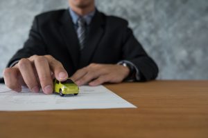 A man in a suit holds a toy car on paper, symbolizing Georgia Lemon Law qualifications and consumer benefits.