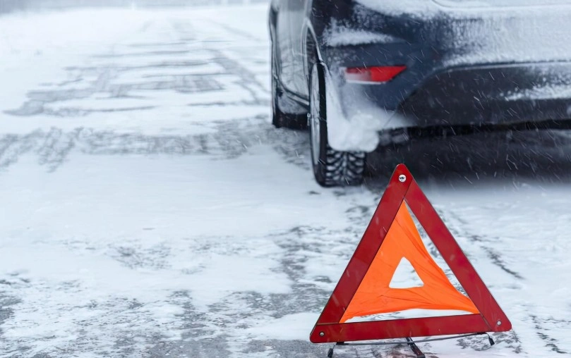 Disabled Dodge vehicle on snowy road with warning triangle representing lemon law claims for defective vehicles The Lemon Reps