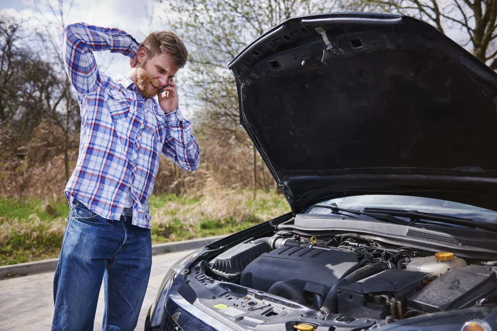 Driver standing beside a disabled vehicle with the hood open, looking frustrated while speaking on the phone about a potential warranty or lemon law vehicle defect.