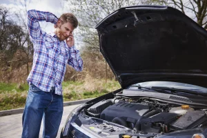 Driver standing beside a disabled vehicle with the hood open, looking frustrated while speaking on the phone about a potential warranty or lemon law vehicle defect.