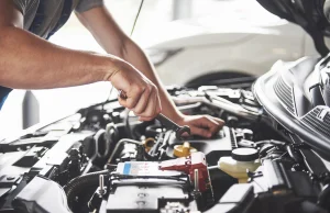 Auto mechanic performing repairs under the hood of a vehicle with a wrench, illustrating repeated repair attempts for a recurring vehicle defect that may qualify under state lemon law protections.