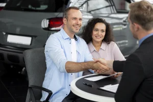 A man and woman shake hands in front of a car, symbolizing a successful vehicle transaction related to Arizona Lemon Law